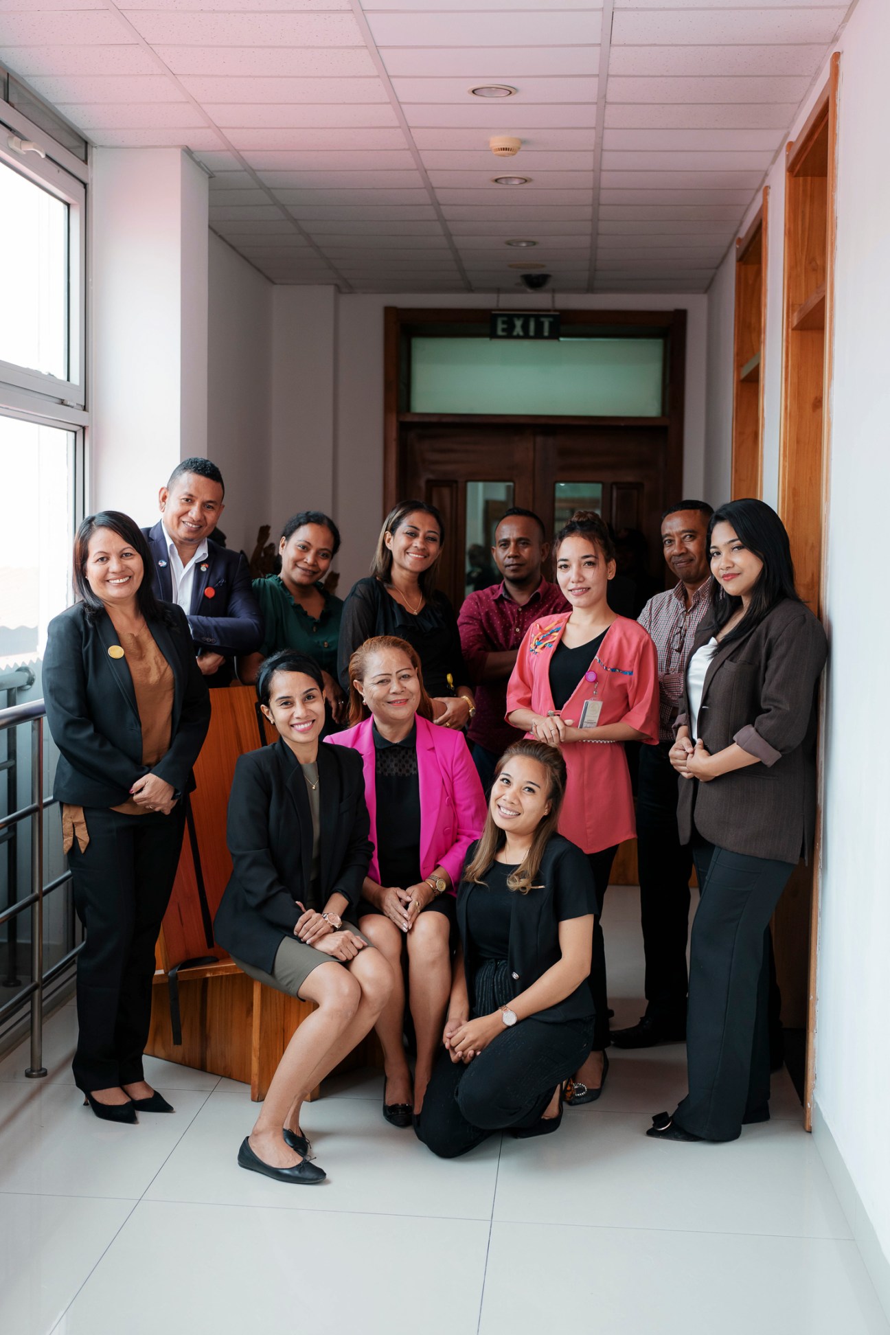 Group of professional staff members posing together in modern office hallway with wooden furnishings