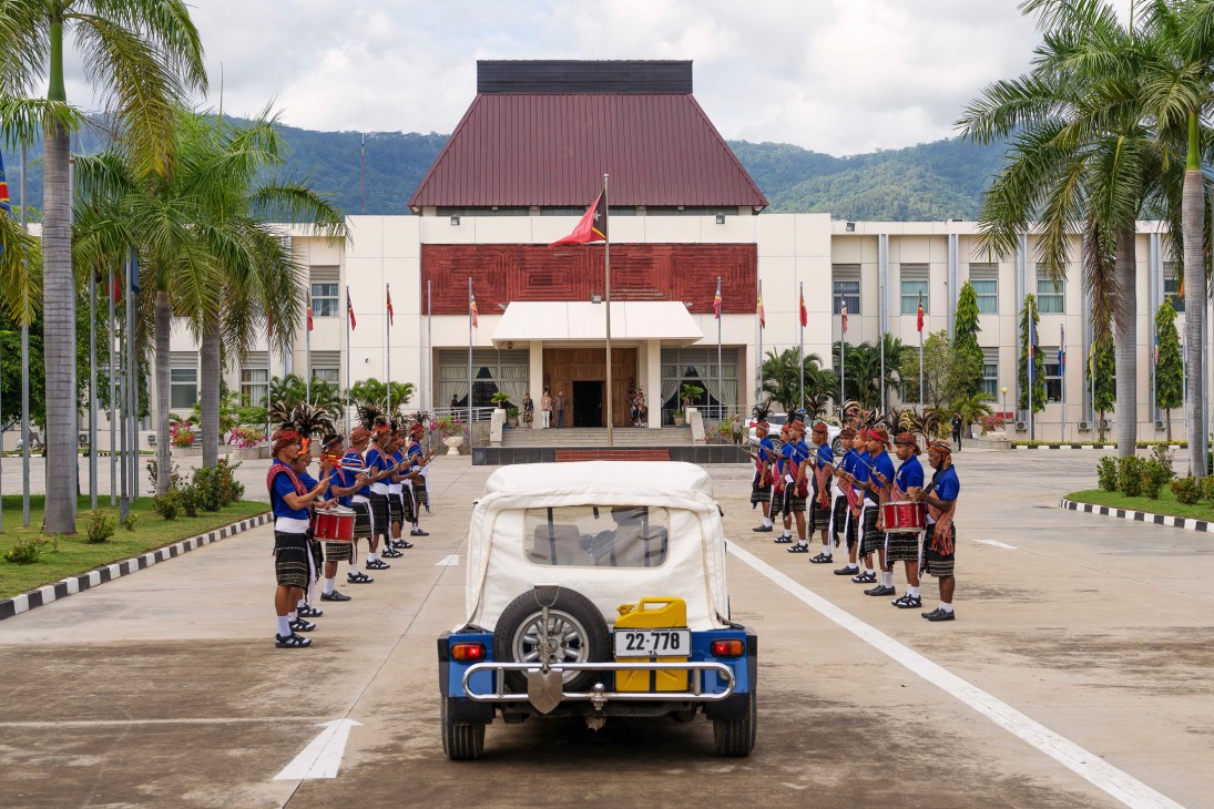 Honor guard in traditional dress flanks white vehicle at presidential palace in Timor-Leste with palm trees