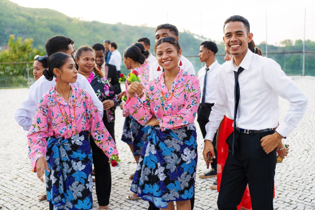 Young people in traditional pink floral tops and blue sarongs smile at a graduation ceremony in Timor-Leste