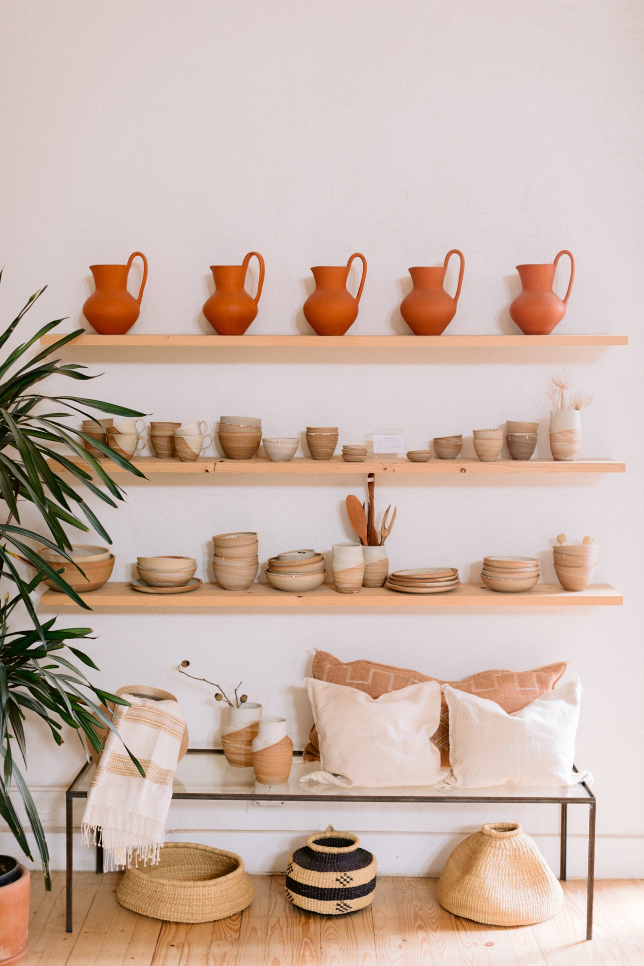 Terracotta pottery vessels and woven baskets displayed on wooden shelves against a white wall.
