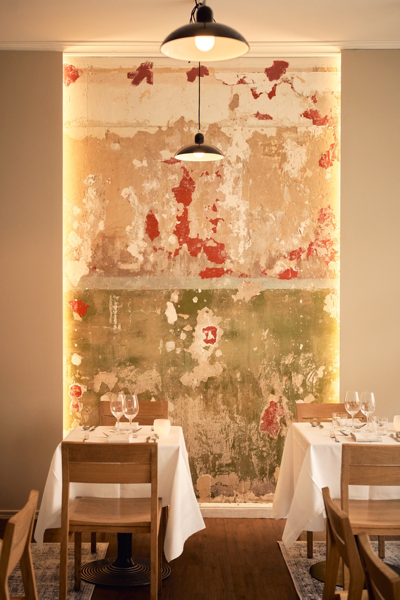 Restaurant dining room with weathered wall, pendant lights, and tables set with white linens and wine glasses