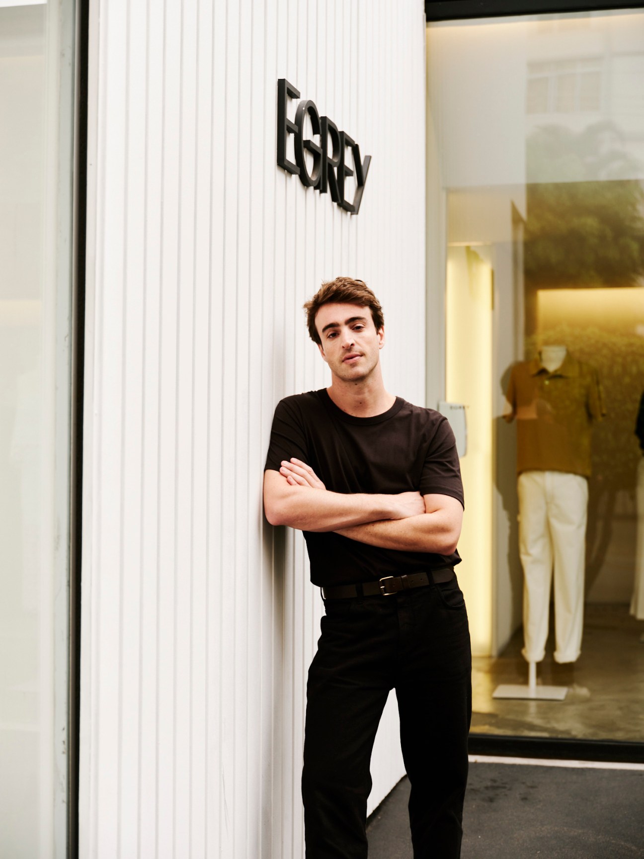 Egrey founder Eduardo Toldi standing with arms crossed wearing black clothing in front of white storefront