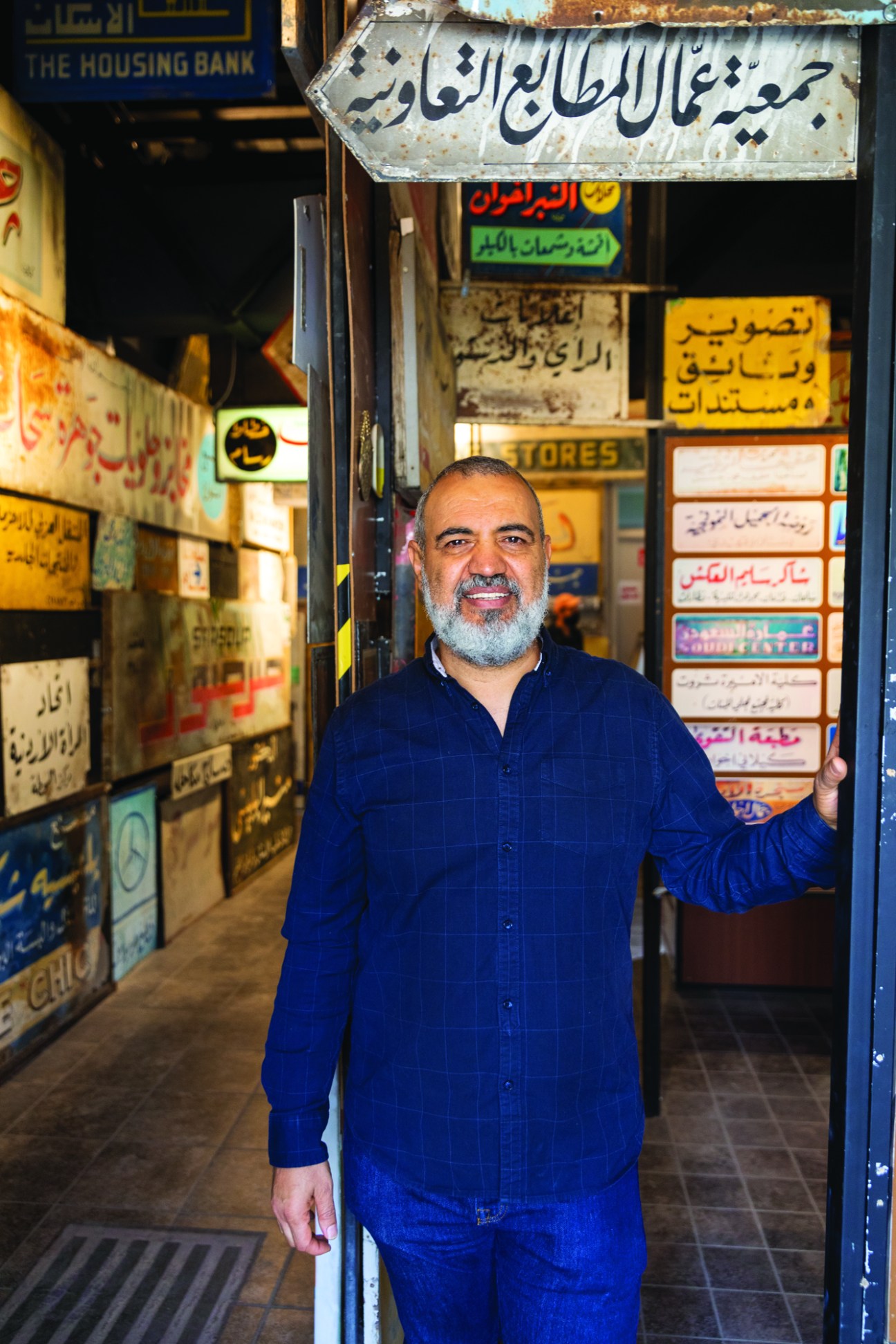 Emad Hajjaj standing in front of a wall covered with Arabic text signs and posters