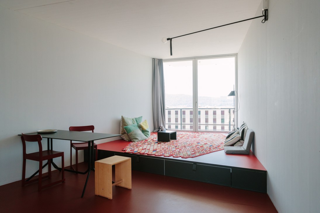 Modern minimalist apartment interior with built-in platform bed, dining table, and large window overlooking urban buildings