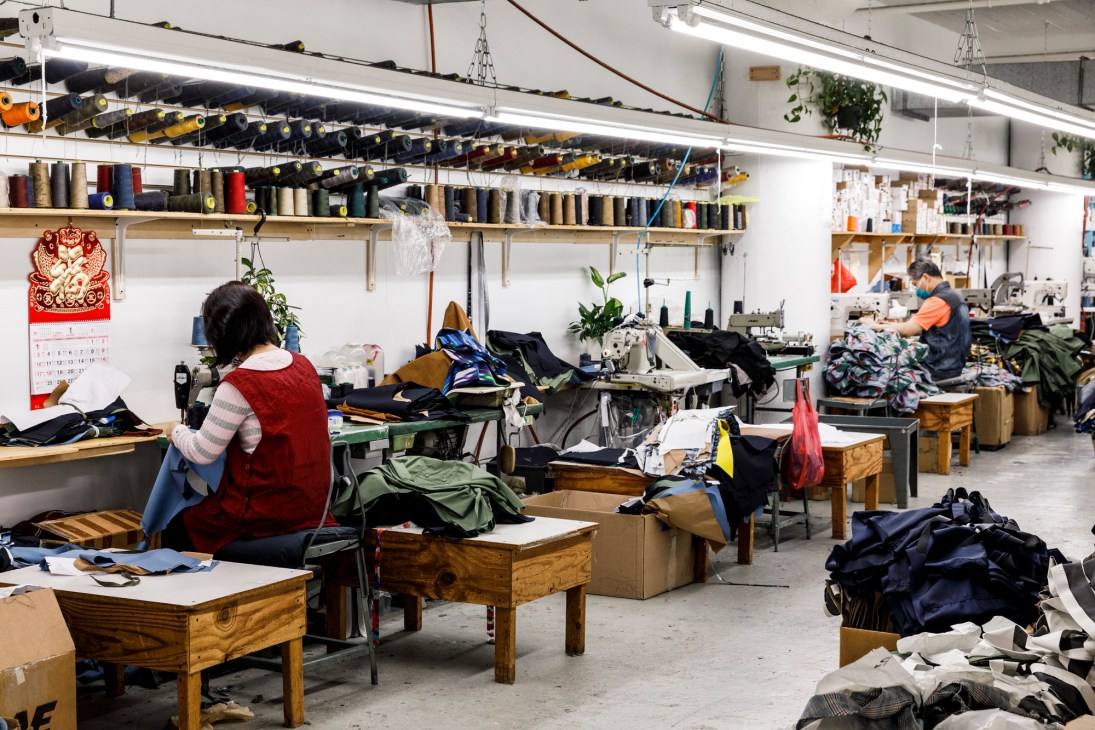 Workers at sewing stations in Engineered Garments' factory in Long Island City with thread spools overhead