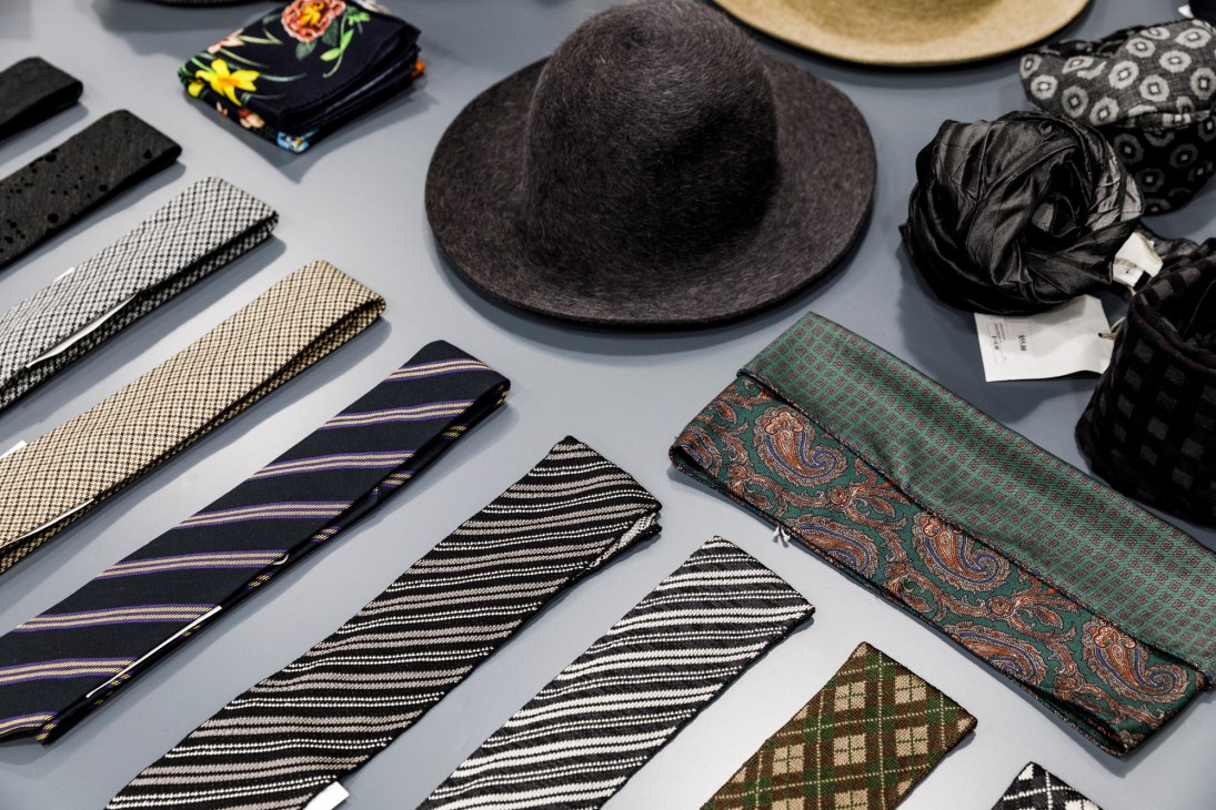 Folded neckties with various patterns including stripes, paisley, and geometric designs arranged on a gray surface