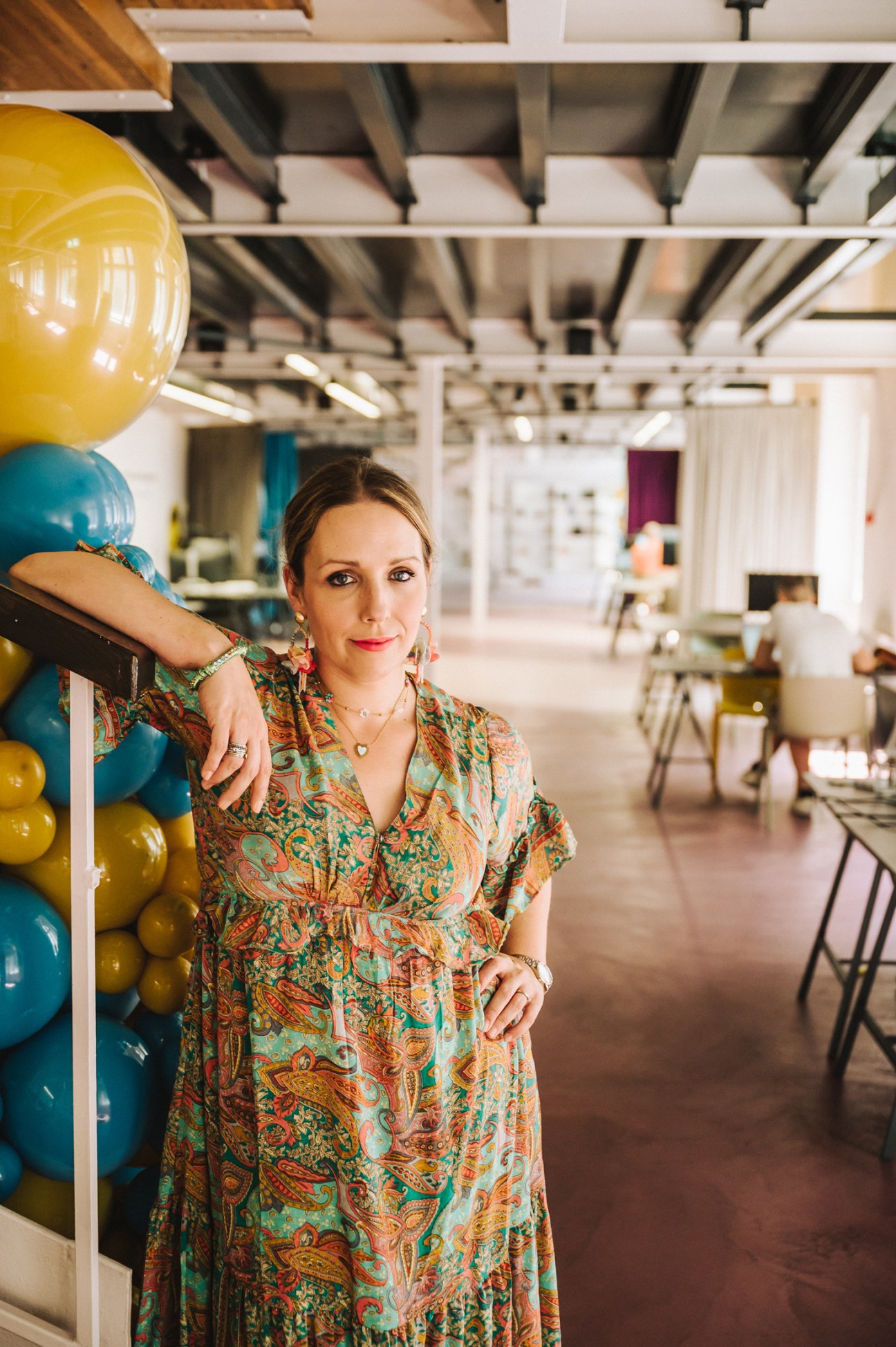 Woman in colorful patterned dress standing in modern office space with exposed ceiling and balloons