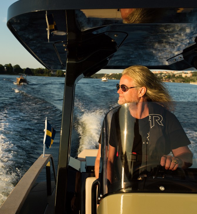 Konrad Bergström with long blonde hair and sunglasses steering an electric boat on water