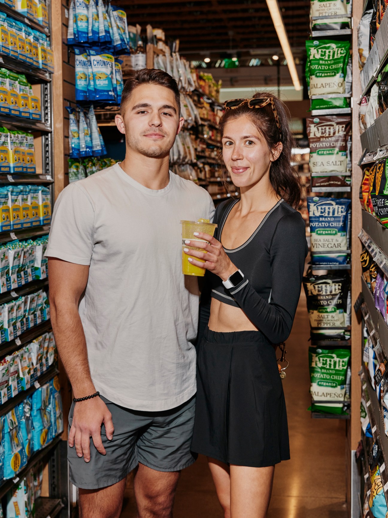 Two people posing together in grocery store aisle holding drinks