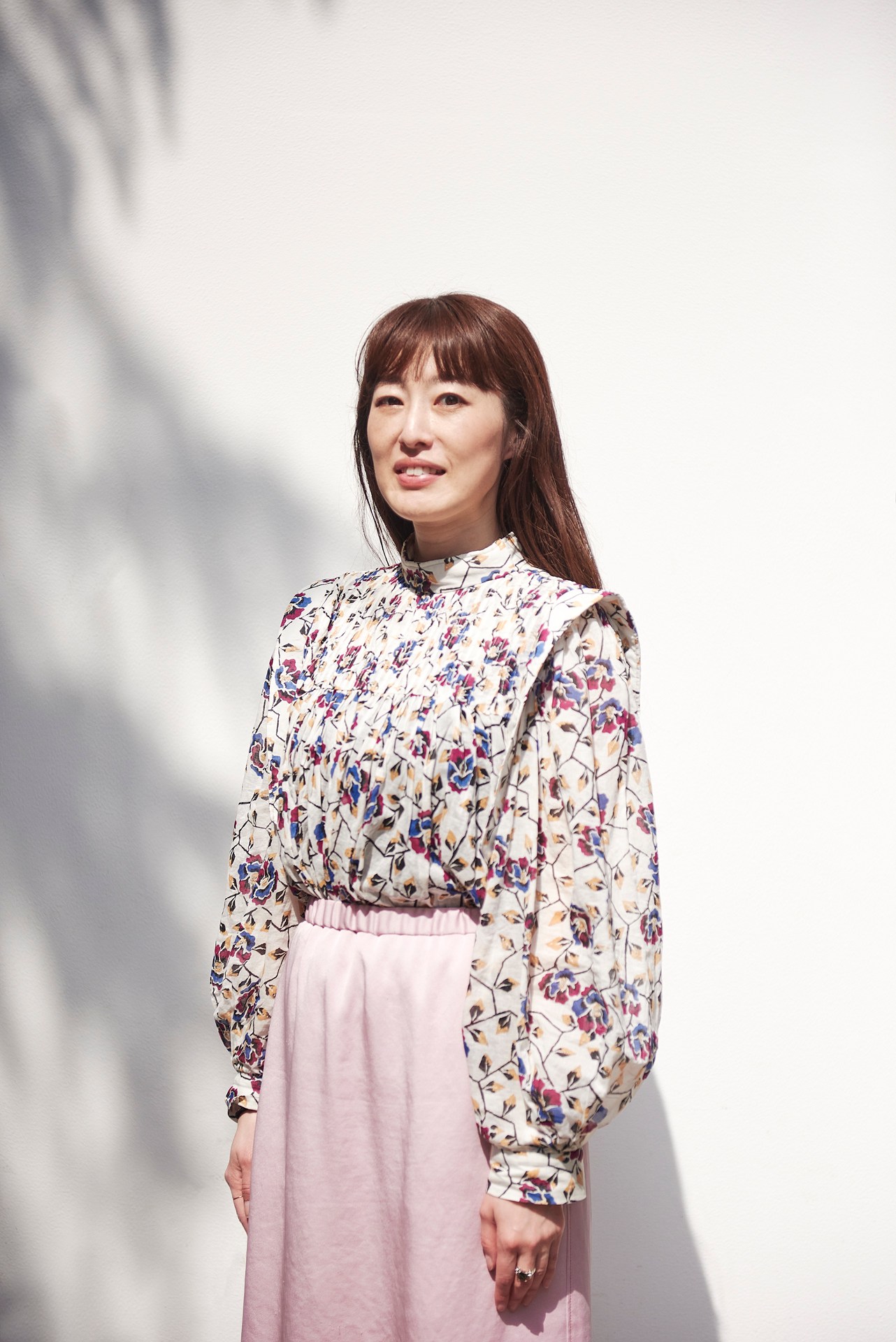 Eri Takane, director of Tokyo Gendai art fair, standing in natural light wearing a floral patterned top.