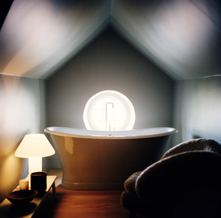 Small bathroom with geometric patterned wall tiles, white bathtub, warm ambient lighting and modern fixtures
