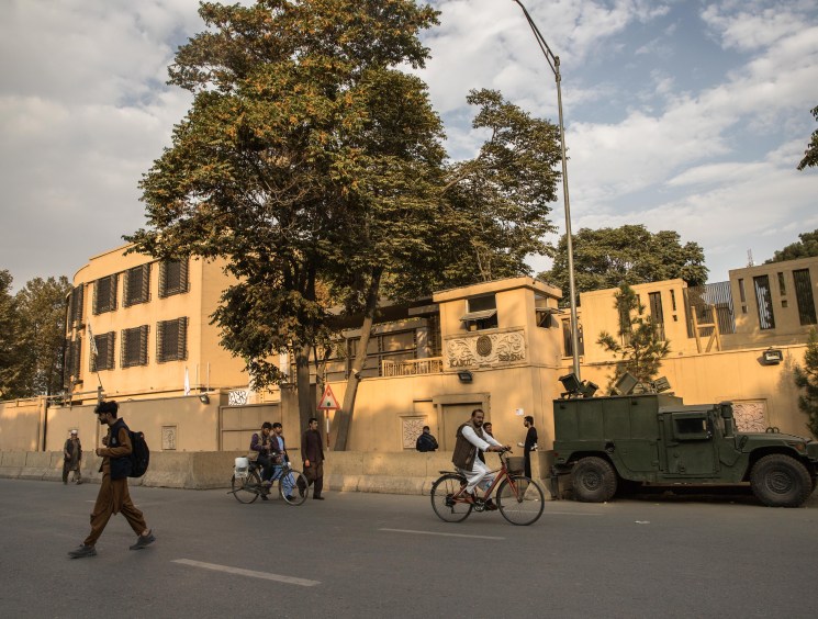 Street scene outside Serena Hotel with Taliban fighters, cyclists, and military vehicle near fortified entrance