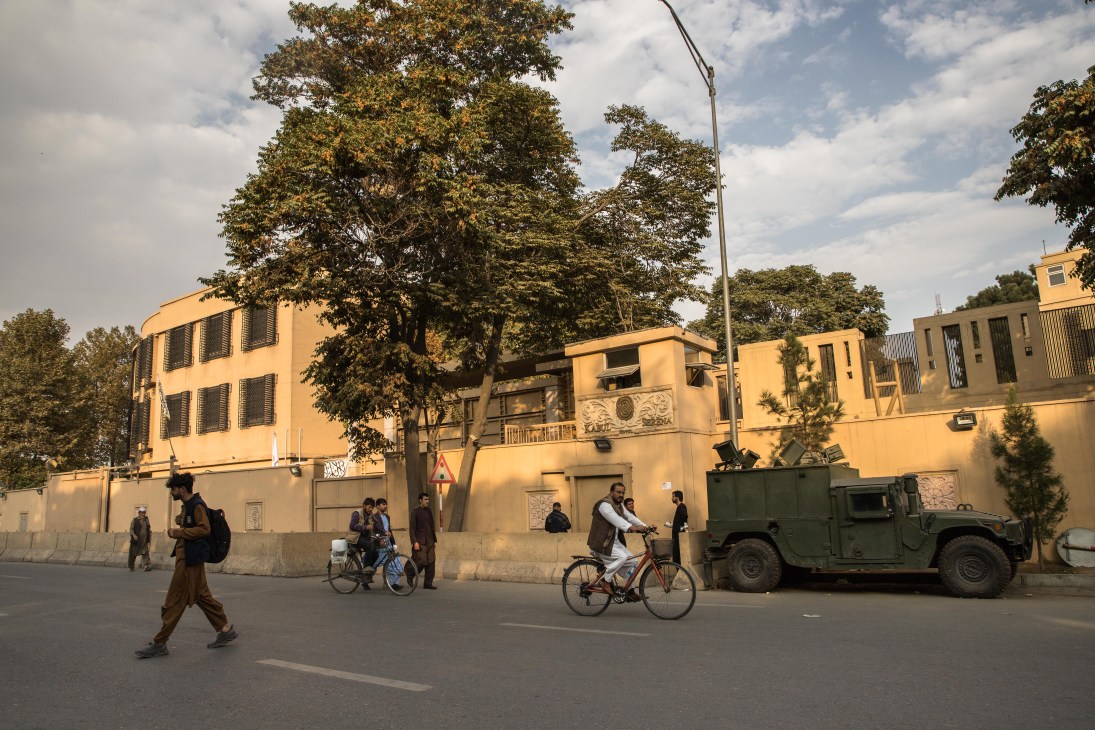 Street scene outside Serena Hotel with Taliban fighters, cyclists, and military vehicle near fortified entrance