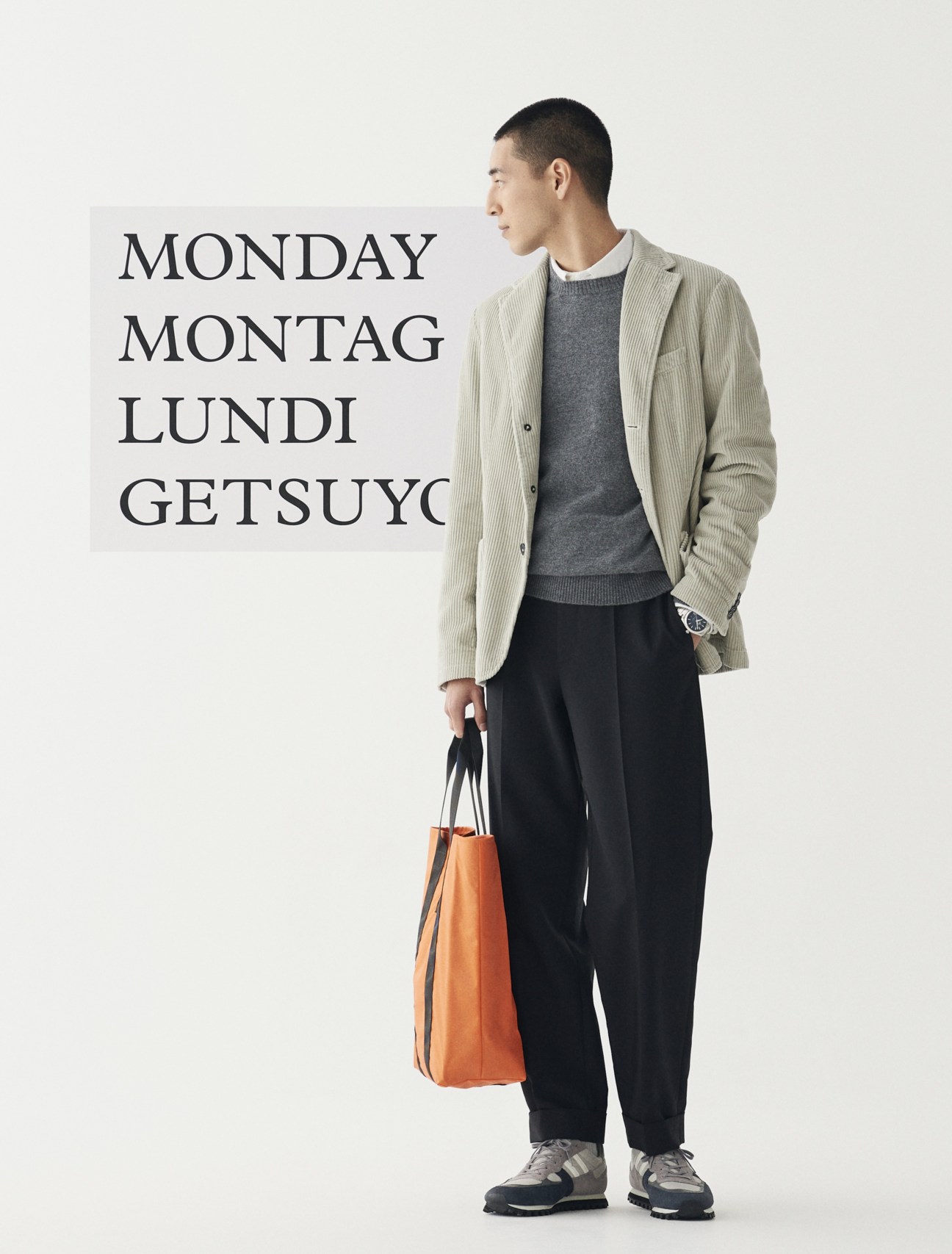 Model wearing beige corduroy blazer, grey sweater, white shirt, dark trousers, grey sneakers and orange leather bag