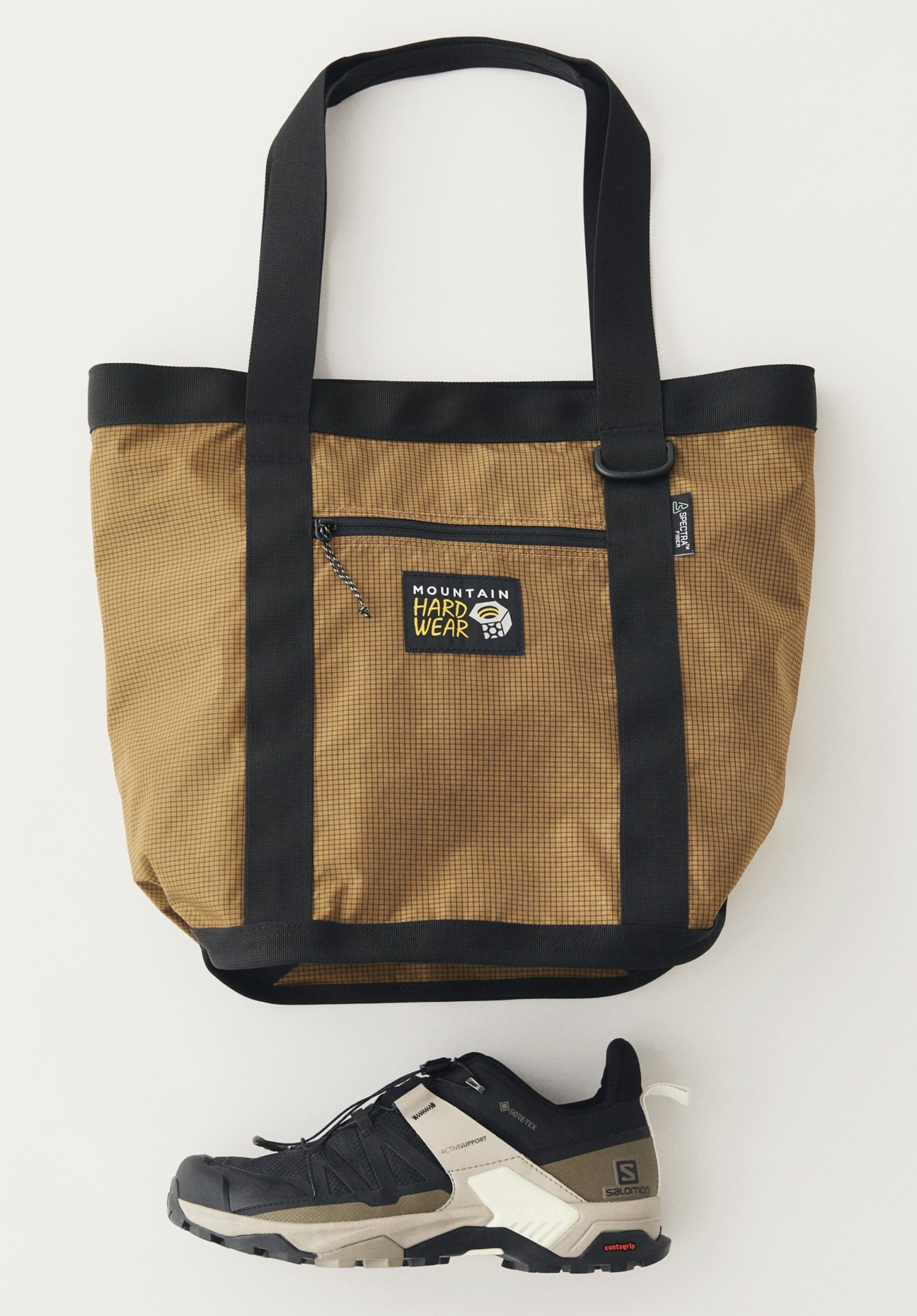 Brown ripstop tote bag by Mountain Hardwear and grey trail running shoe by Salomon on white background