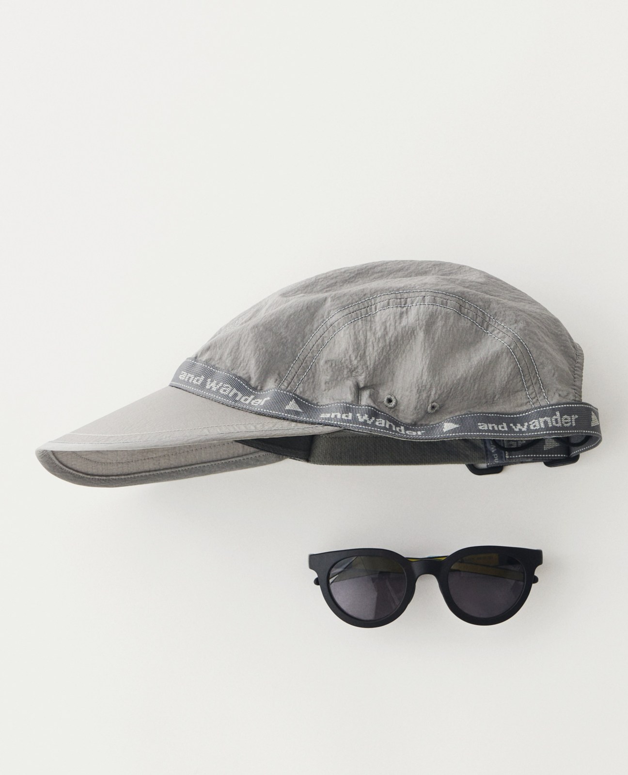 Grey baseball cap and black sunglasses arranged on white surface