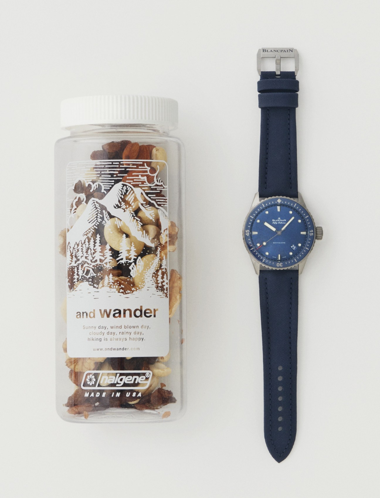 Blue dive watch with navy strap next to clear water bottle with trail mix and mountain graphics