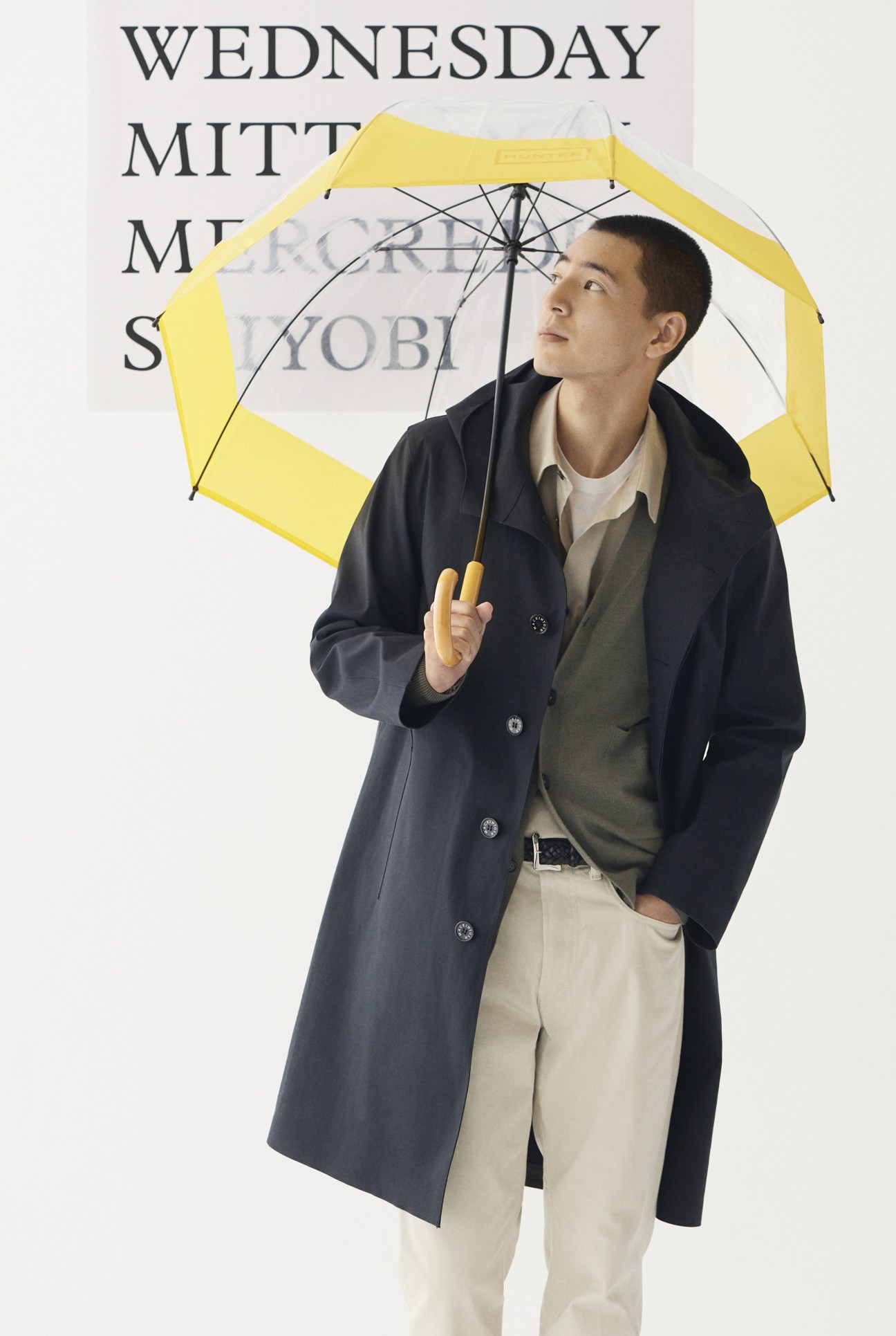 Model in navy coat, grey cardigan, white shirt, navy t-shirt and jeans with umbrella