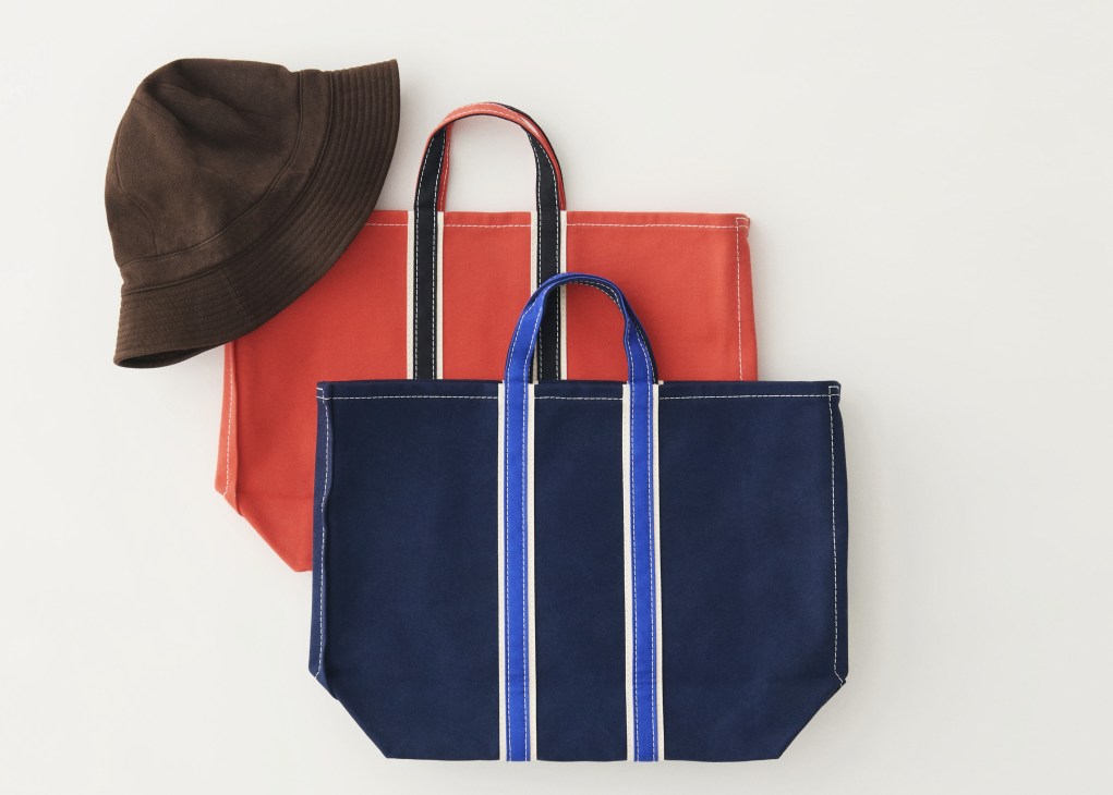 Brown bucket hat and canvas tote bags in navy and coral red arranged on white surface