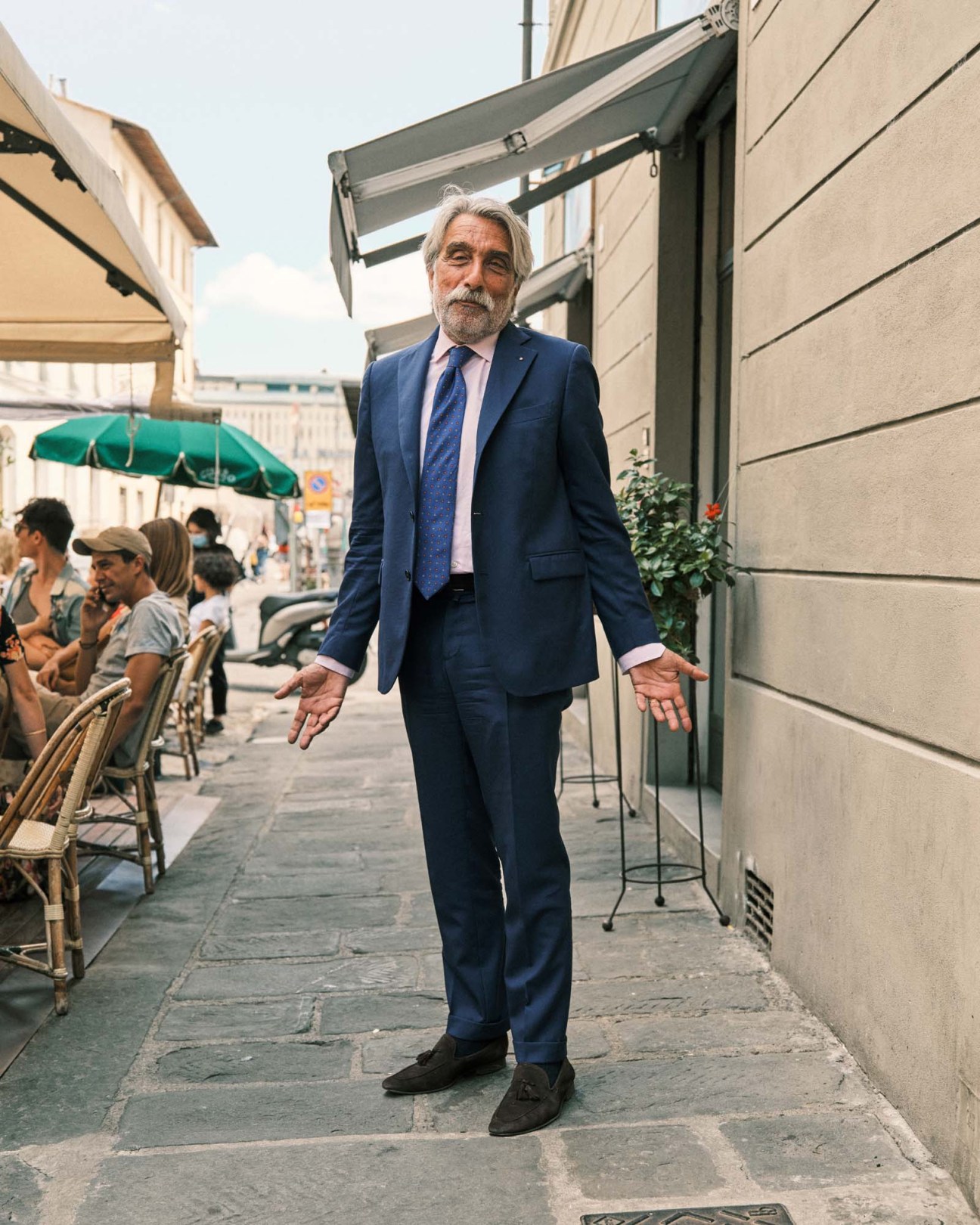 Man in navy suit and blue tie standing on Florence street with outdoor café seating