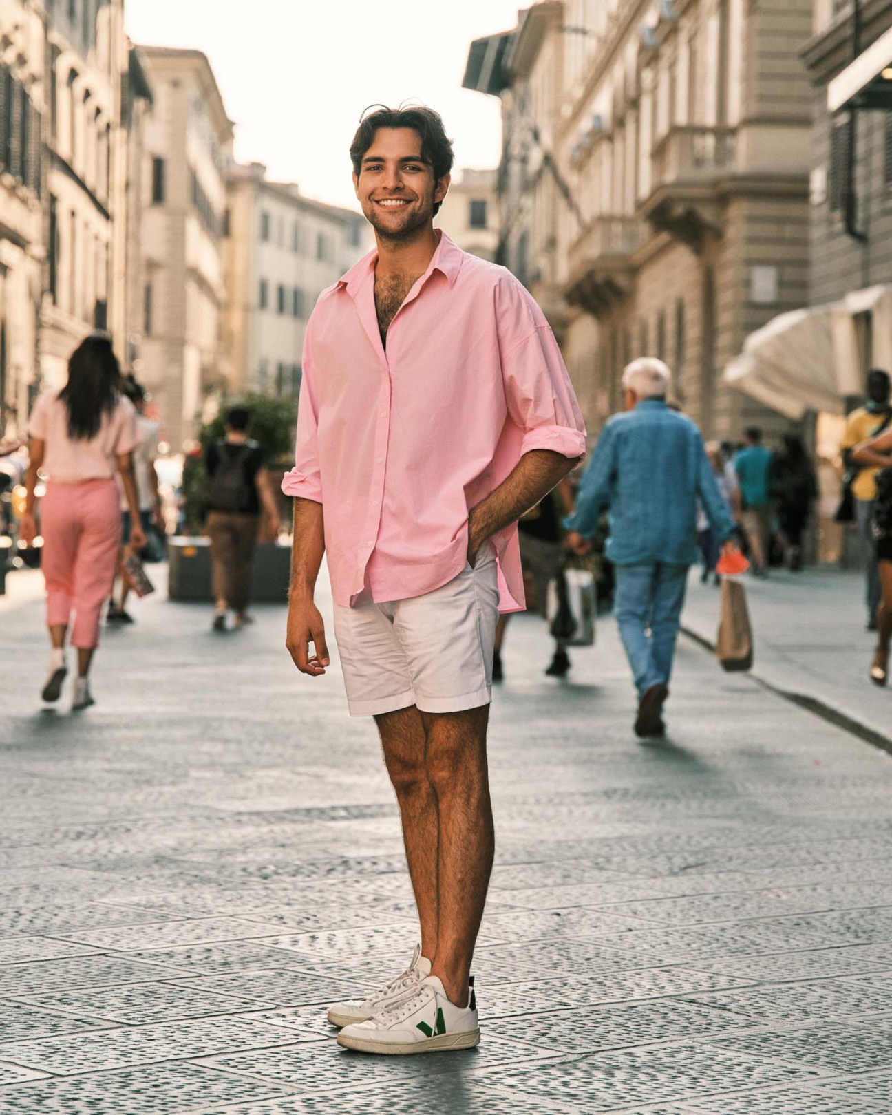 Man in pink button-up shirt and white shorts standing on a Florence street lined with Renaissance buildings.