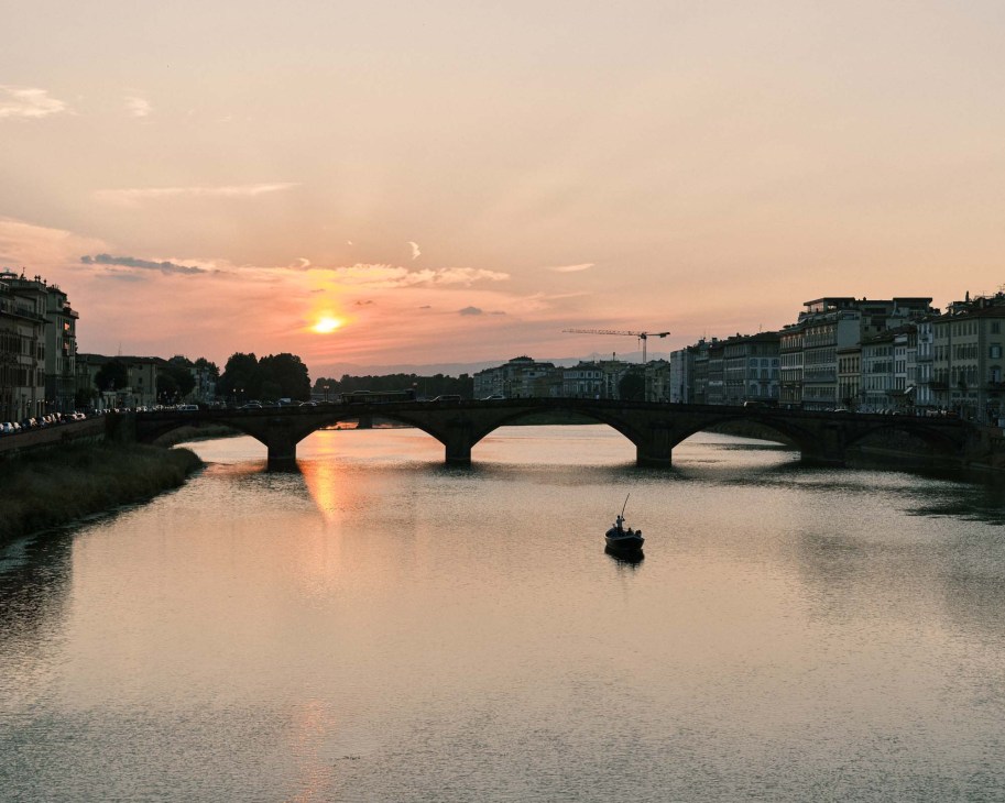Sunset over the Arno River in Florence with Ponte Vecchio and historic buildings reflected in the water.