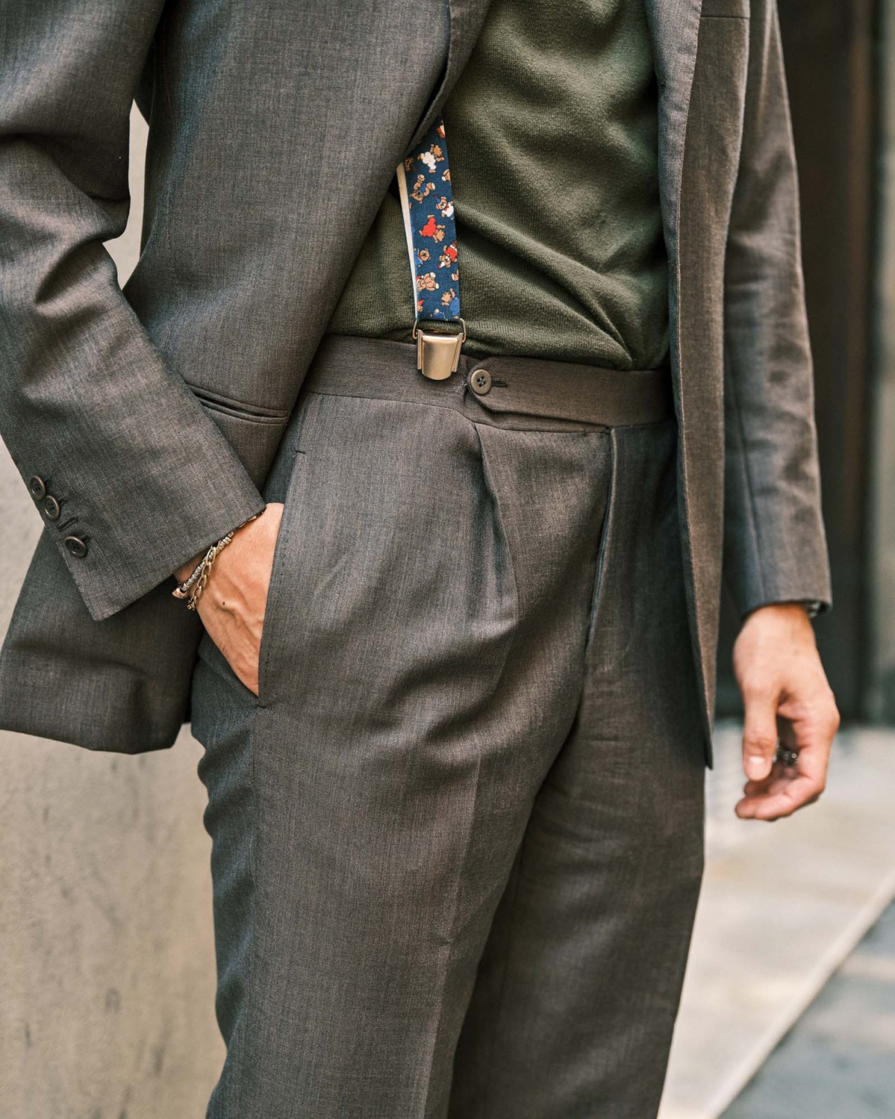 Close-up of a man's torso wearing a grey suit jacket with a blue floral patterned suspender and gold buckle.