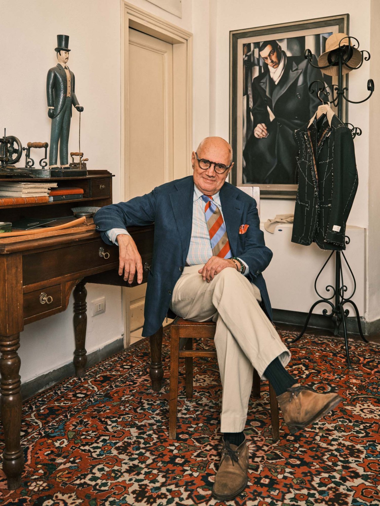 Master tailor Antonio Liverano seated in his Florence atelier surrounded by tailoring tools and garments on display.
