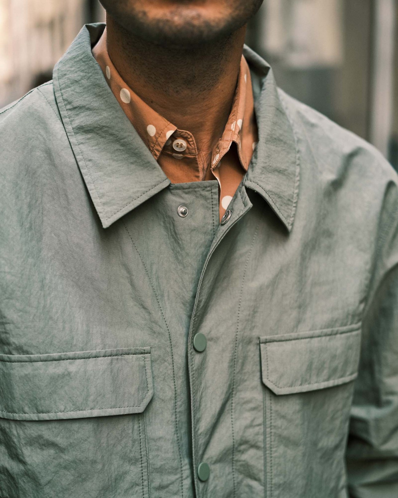 Man wearing a sage green button-up shirt with visible collar detail and decorative buttons.