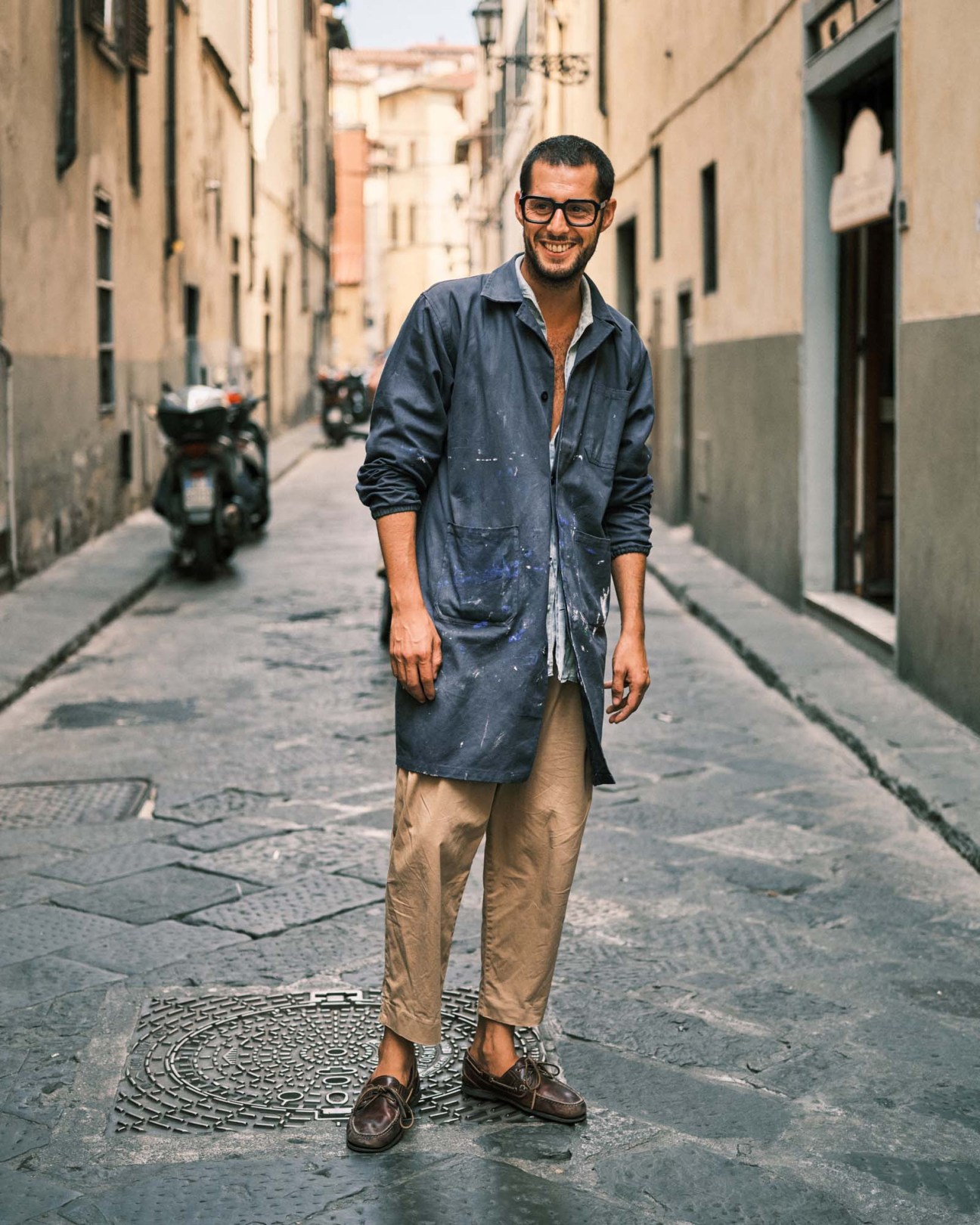 Man in denim shirt and beige trousers standing in a narrow Florence street with historic buildings.