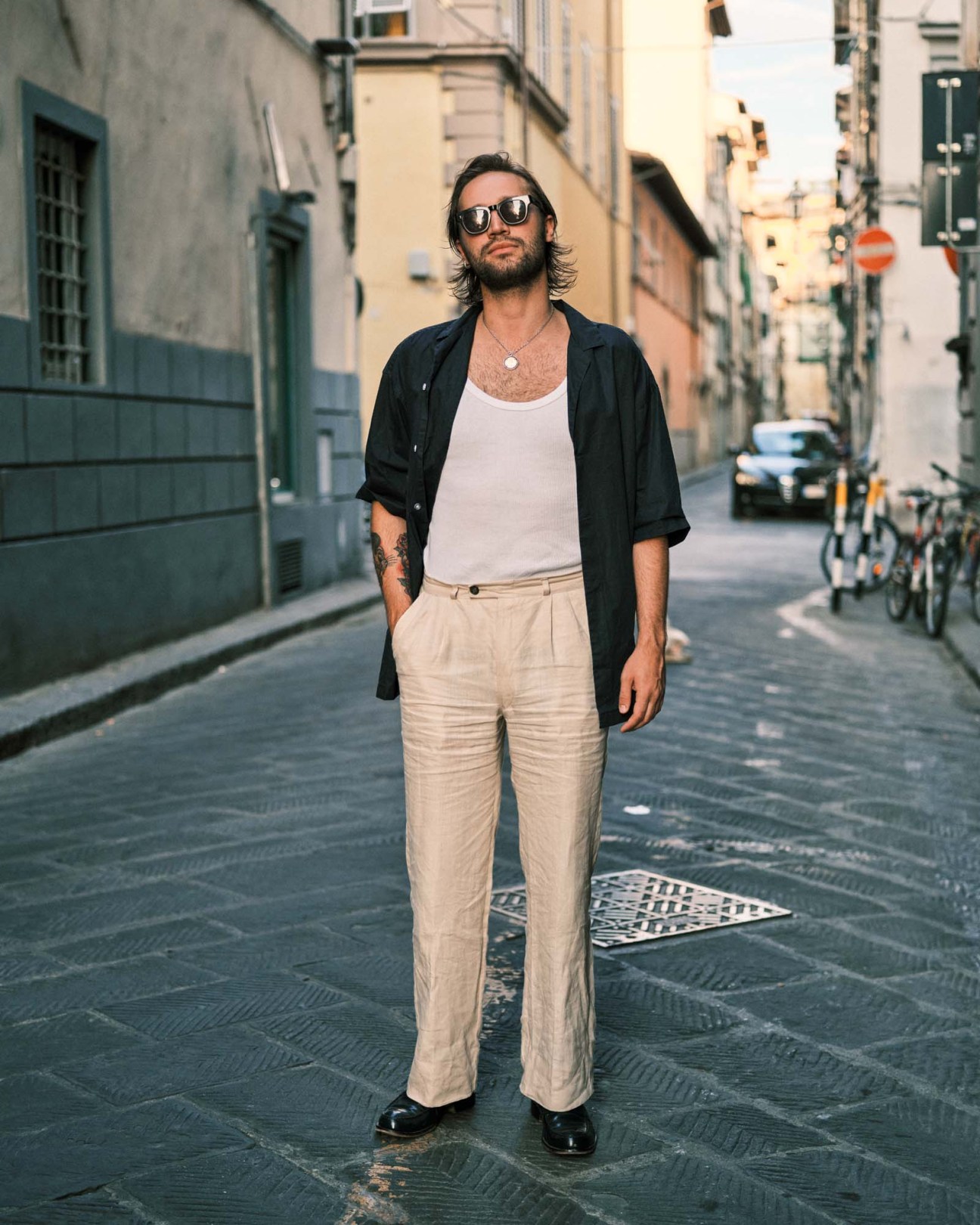 Man in sunglasses wearing black shirt and cream trousers standing on Florence street.