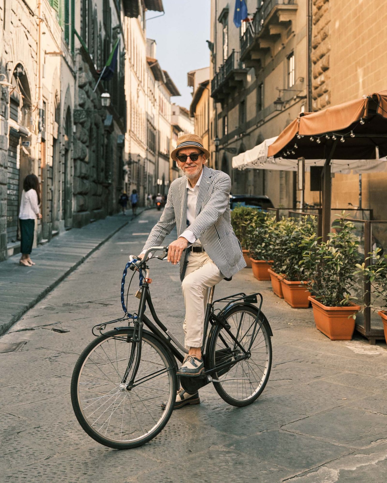 Man on bicycle in striped blazer and hat on Florence street with orange awnings