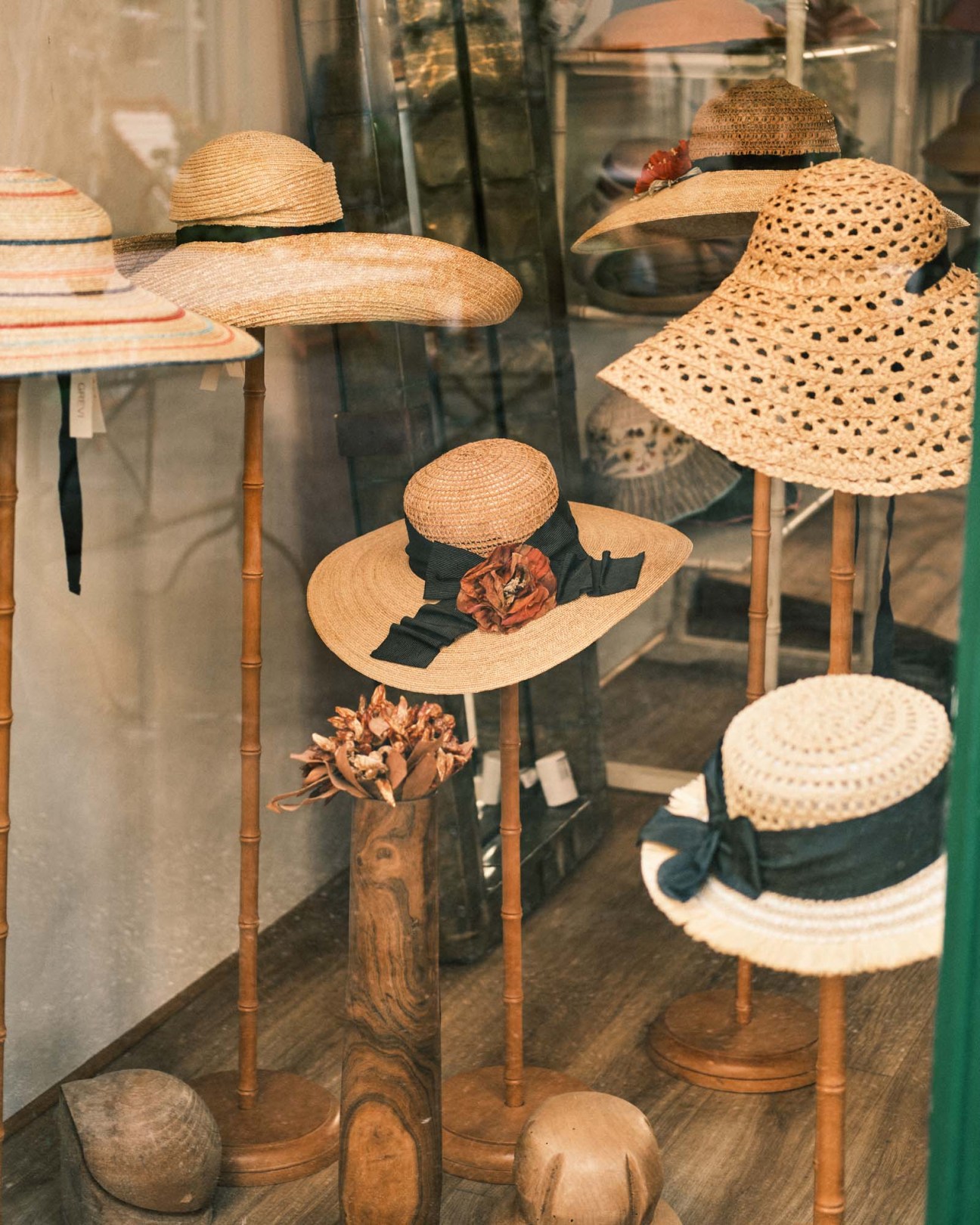 Display of straw hats with various weaves and styles on wooden stands in a shop window.