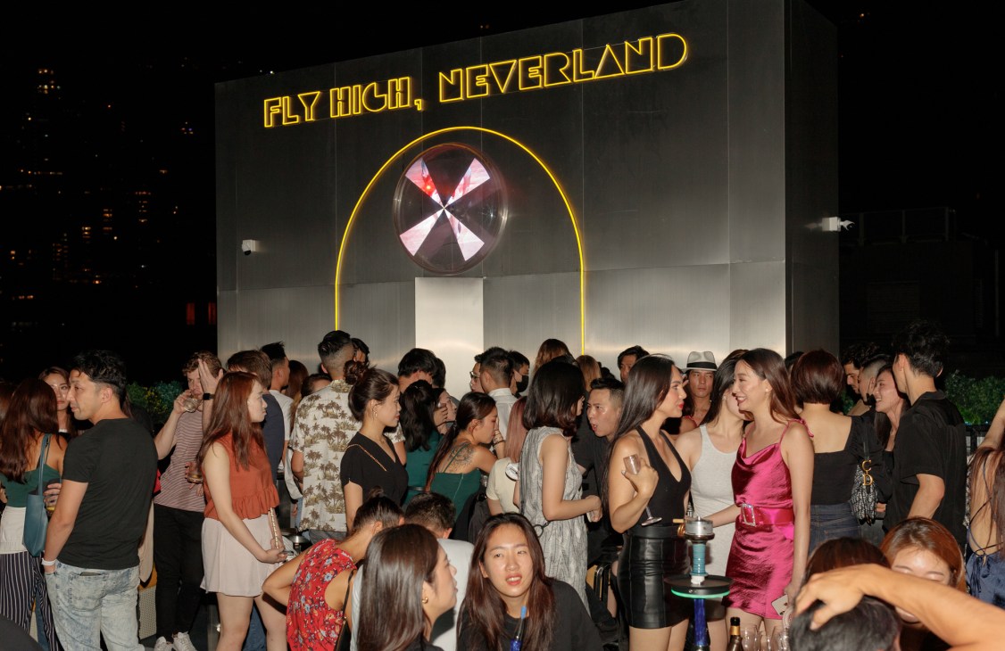 Crowd of people gathered at Faye nightclub in Hong Kong with neon signage reading 'Fly High, Neverland' above them.