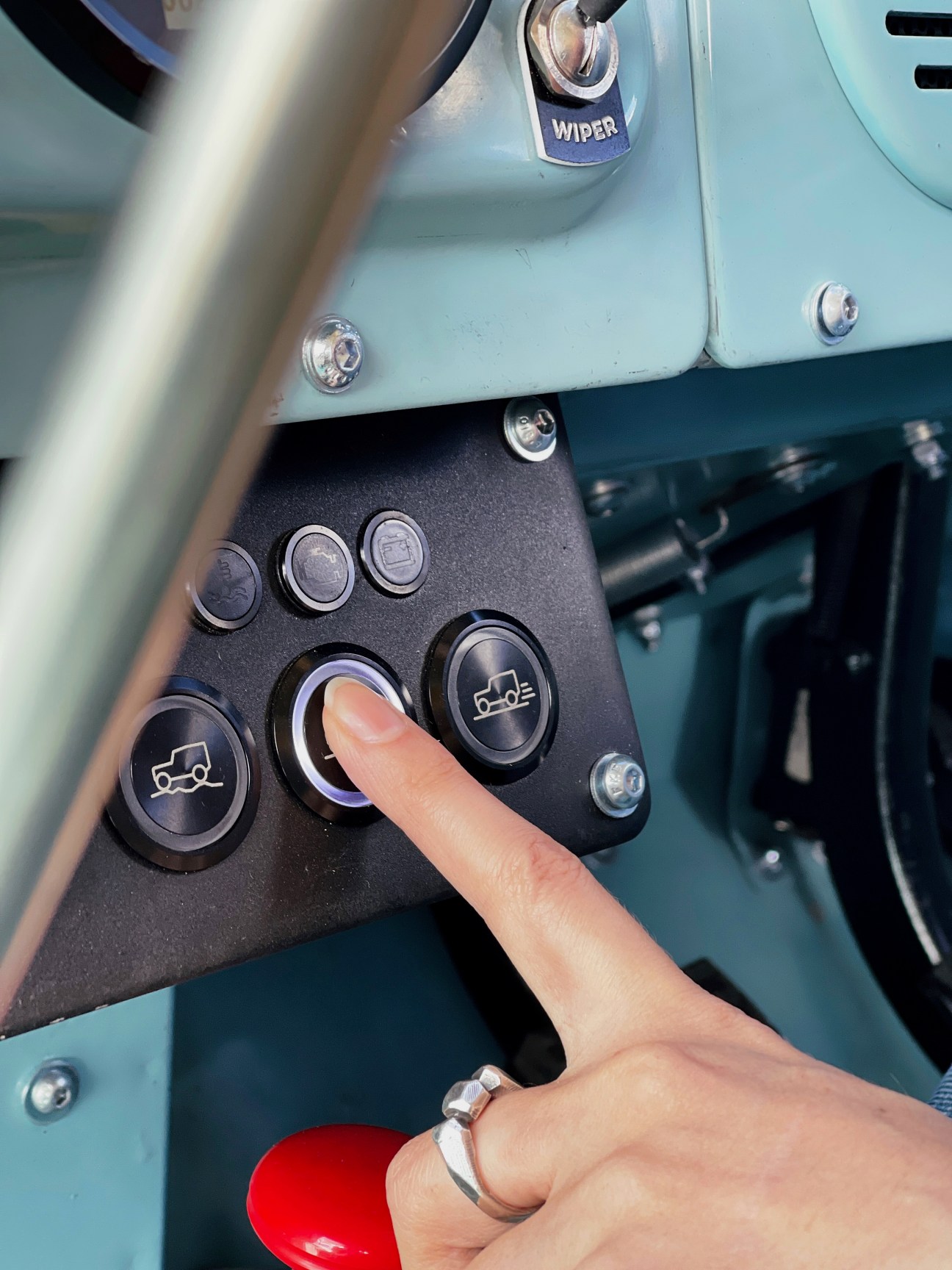 Hand pressing button on control panel of converted electric Land Rover showing dashboard interface