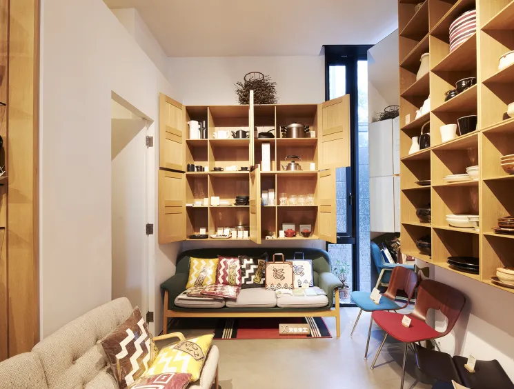 A cosy homeware shop interior with light wood shelving displaying ceramics, with a colourful sofa and cushions at the centre.