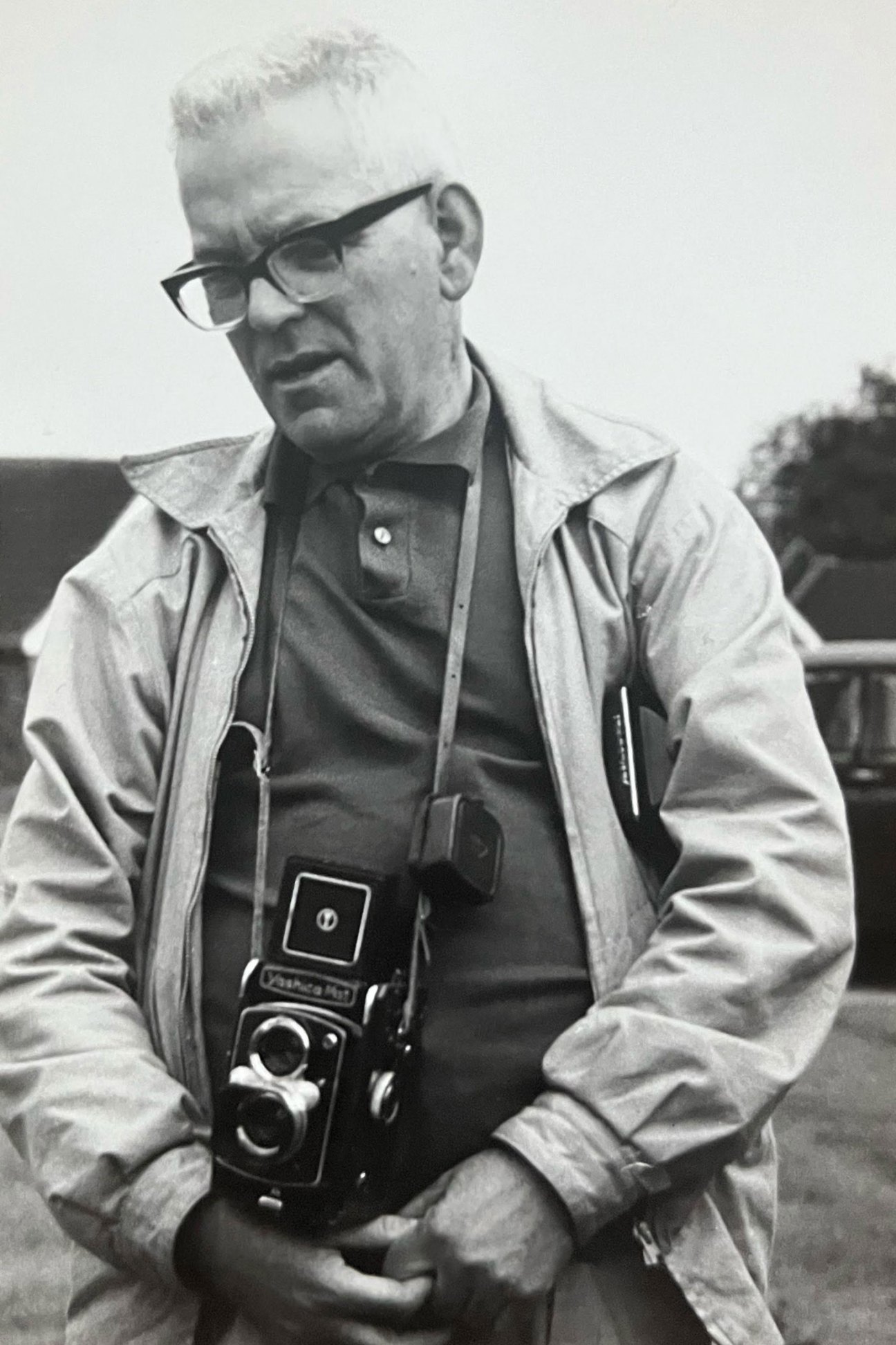 Young John Balsom as a child in casual clothing standing outdoors in the 1970s with glasses holding a twin-lens reflex camera, wearing a light jacket