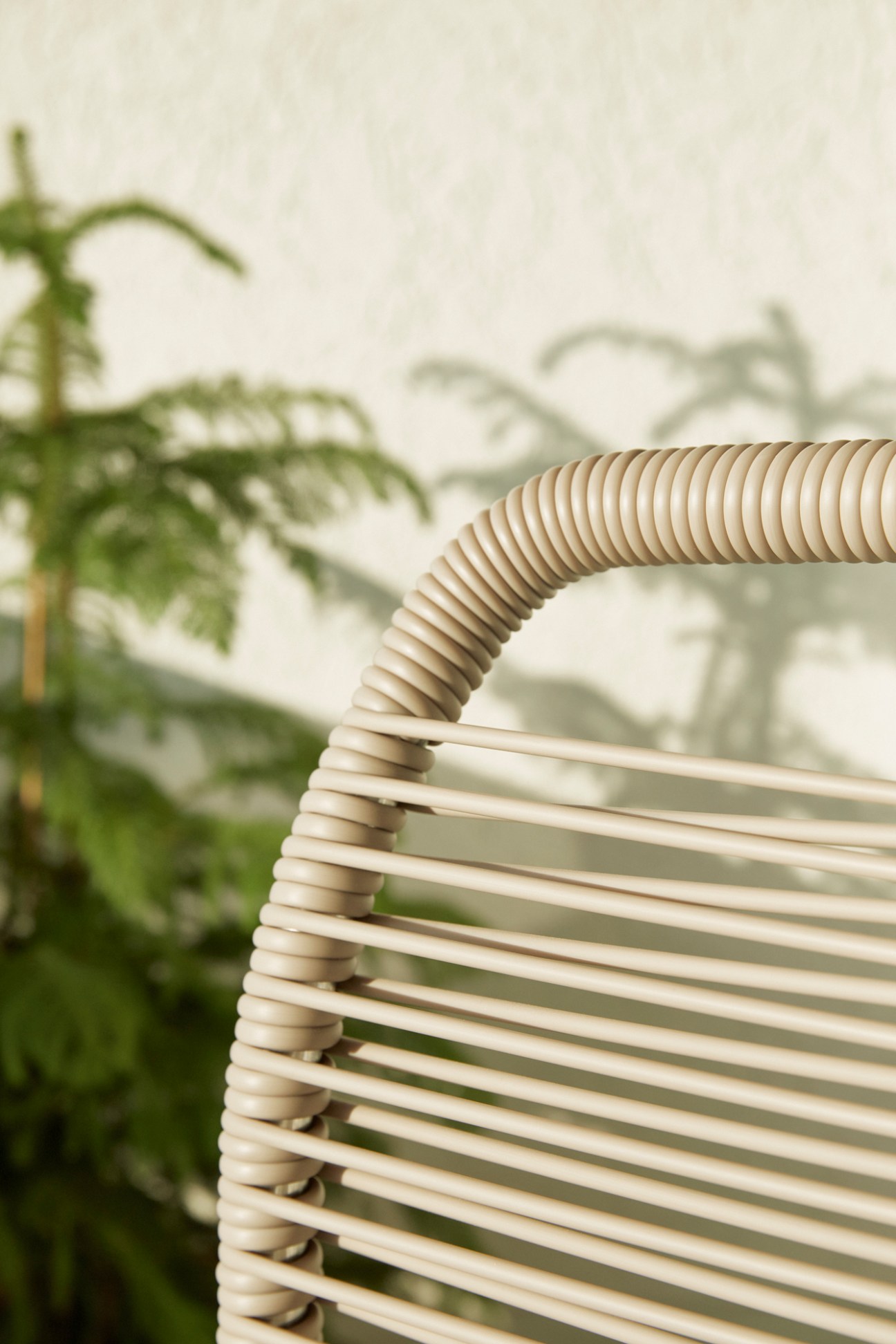 Close-up detail of Fiam's Spaghetti deck chair showing its distinctive woven cord design with blurred greenery in background.