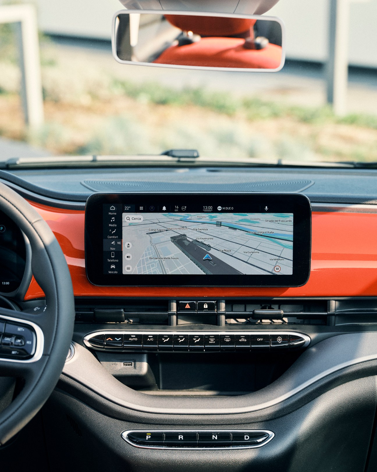Interior view of a red Fiat 500e displaying navigation map on touchscreen display with steering wheel and dashboard controls visible.