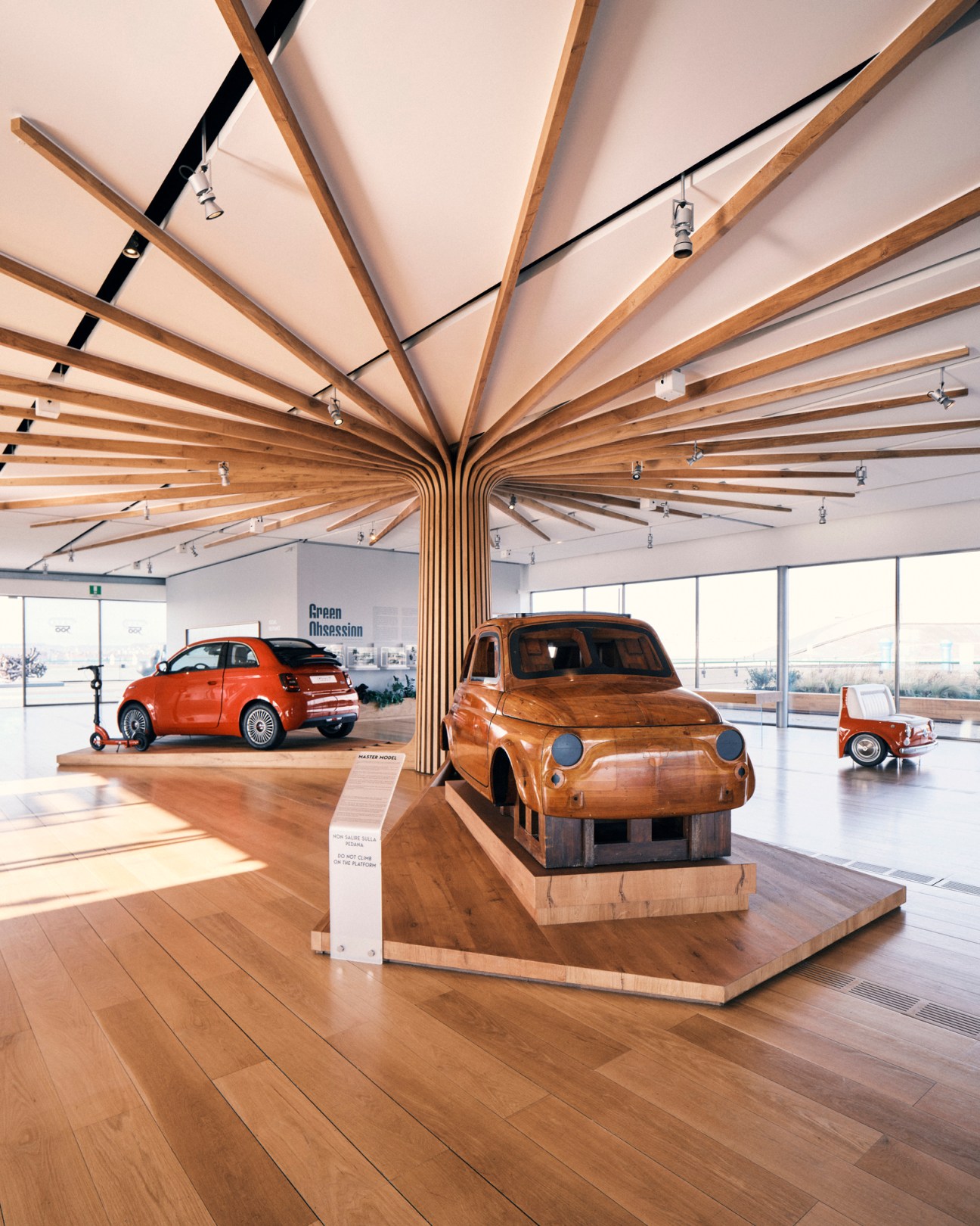 Interior of La Casa 500 museum displaying wooden car sculptures under geometric wooden ceiling beams.
