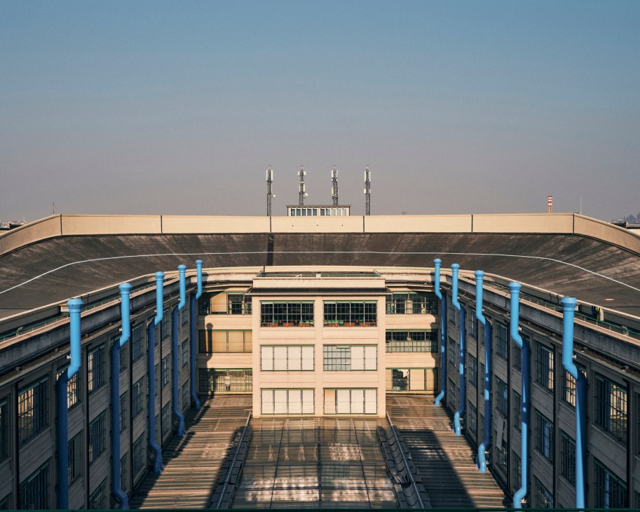 The Lingotto building's rooftop test track with curved concrete and blue support columns under clear sky.