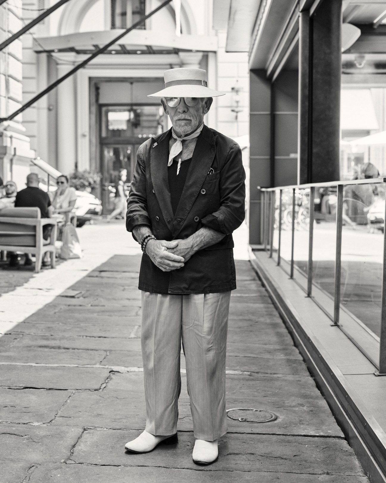 Elderly man in white hat and dark blazer standing confidently on urban sidewalk