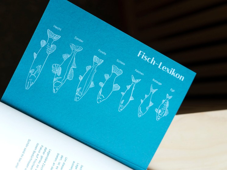 A blue card or menu showing illustrated fish types labeled in German, titled 'Fisch-Lexikon'