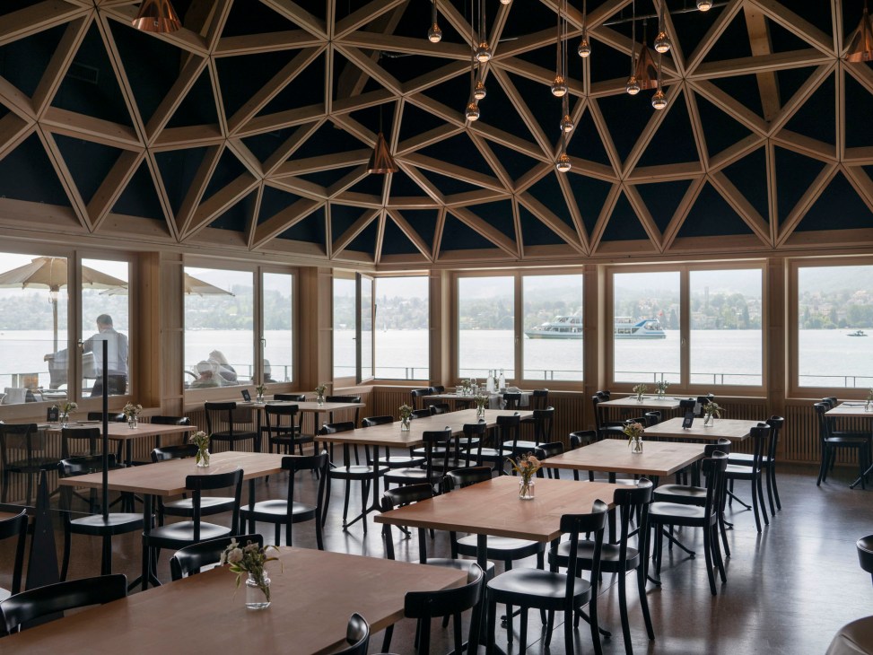 Interior view of the Fischerstube dining room showing the distinctive geometric wooden ceiling and large windows overlooking the lake