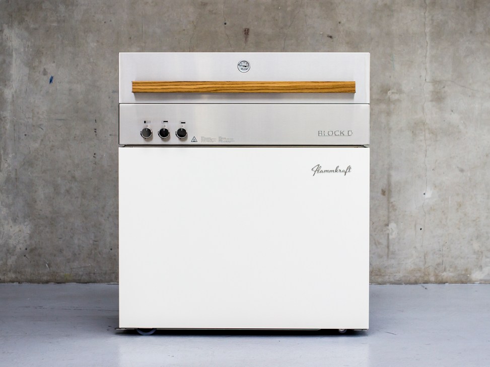 White Flammkraft Block D grill with wooden handle and control knobs against concrete wall