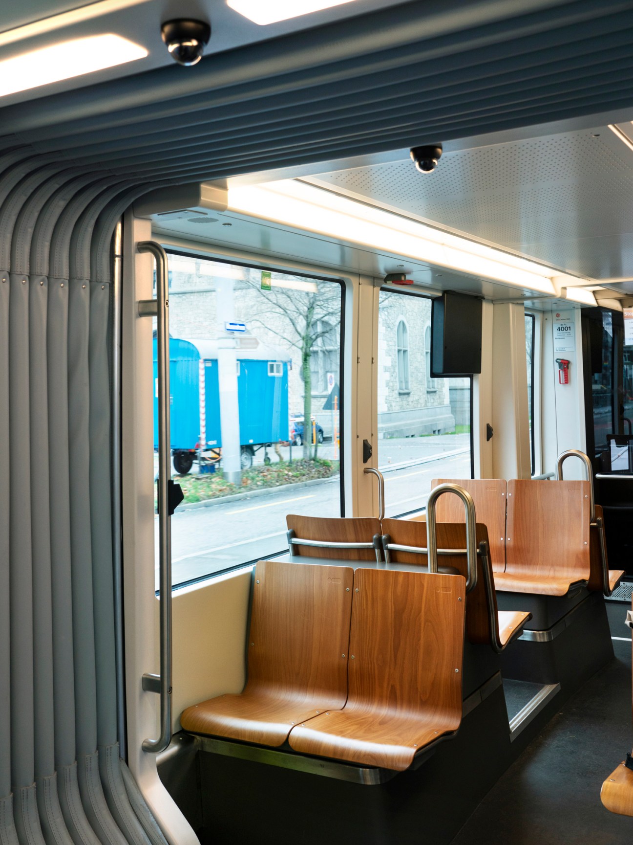 Interior of a Zürich Flexity tram showing wooden seats and large windows with city views.