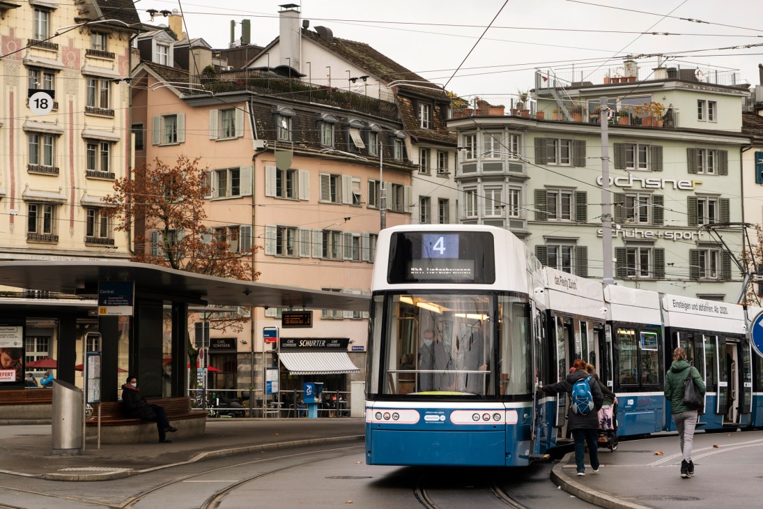 A blue and white Flexity tram numbered 4 stops on a Zürich street lined with historic buildings.