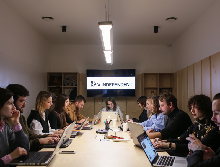 Team members of the Kyiv Independent working at a long table in their office with a monitor displaying the publication's logo.