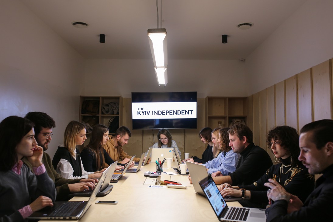 Staff members of The Kyiv Independent working at laptops around a conference table in their newsroom