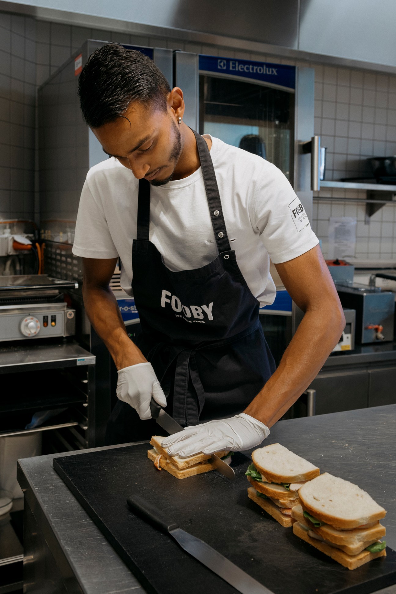 Chef in Fooby apron preparing sandwiches at professional kitchen counter